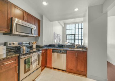 Upgraded kitchen in a Center City apartment with brown cabinets and stainless steel appliances with view of the living area at The Packard
