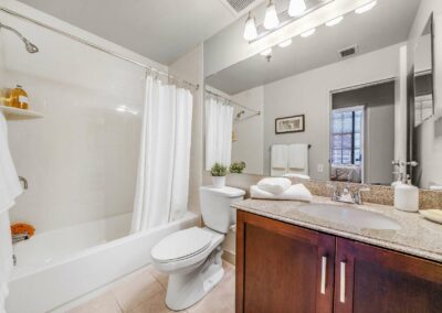 Center City apartment bathroom featuring white tub and shower combination, granite countertop vanity.
