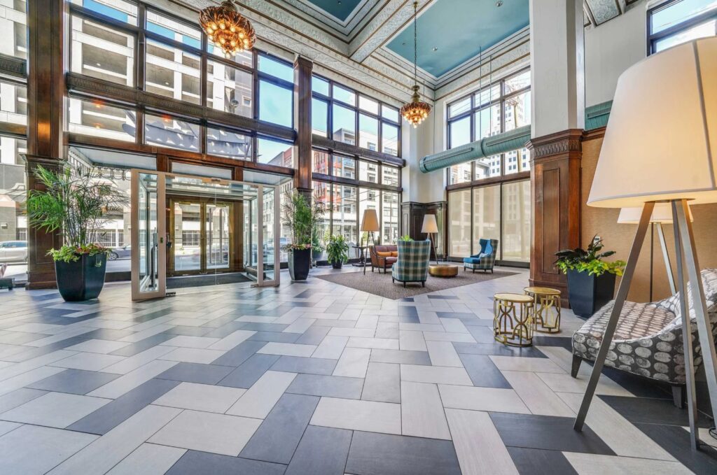 Spacious hotel lobby with large windows, modern tile flooring, seating areas, potted plants, and decorative lighting fixtures.