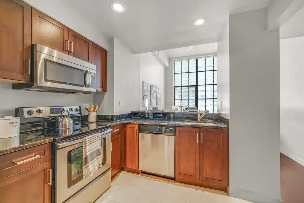 Modern kitchen with stainless steel appliances, dark granite countertops, brown cabinets, and a large window letting in natural light.